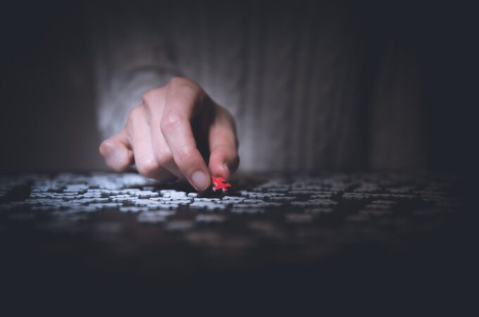 A hand holds a red puzzle piece over grey pieces on a table.