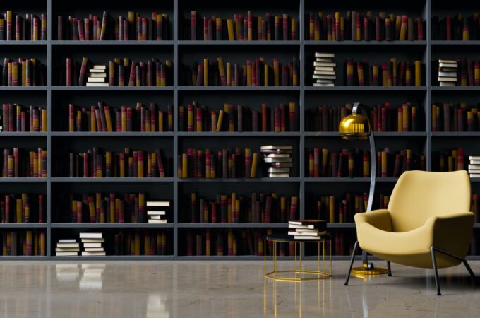 an empty arm chair with a lamp beside it in front of a bookcase that extends along the wall