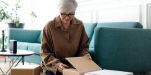 An older woman is packing boxes in her living room.