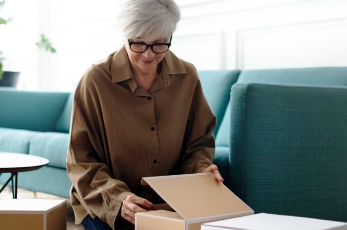 An older woman is packing boxes in her living room.