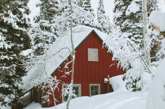 A red house buried in snow up to the bottom of the window.s